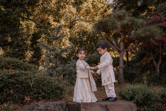A boy in an ivory sherwani and girl in ivory lehenga posing amongst trees